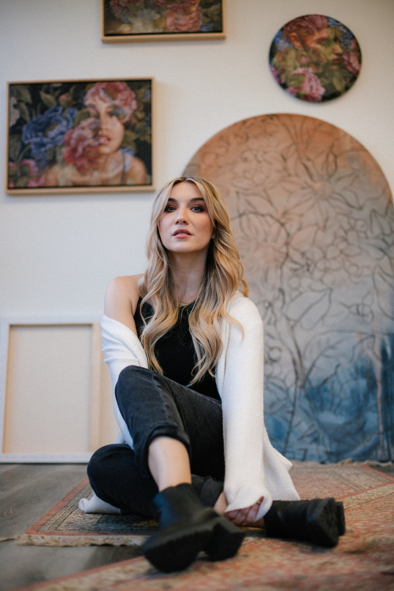 Jess Currier, Los Angeles-based painter, sitting in her studio surrounded by her modern romantic art.